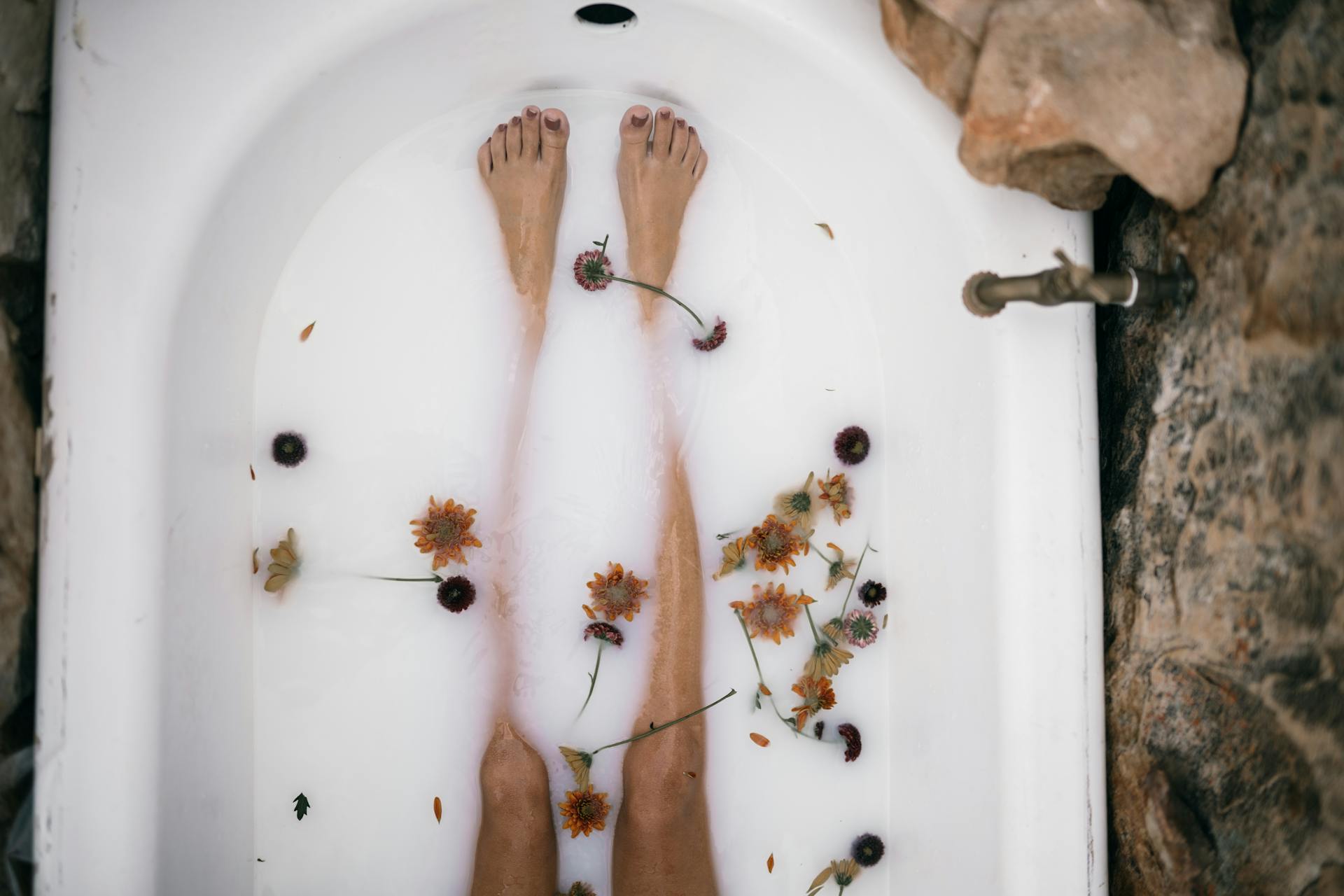 Woman in a bathtub with milky water, flowers, natural stone
